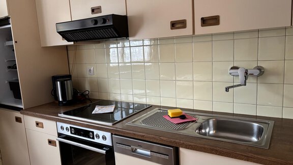 Eine moderne Küche mit einem Herd, einem Backofen und einer Spüle. Die Wände sind mit hellen Fliesen verkleidet und es gibt eine Kaffeemaschine auf der Arbeitsplatte. - Apart Resi - Niederthai