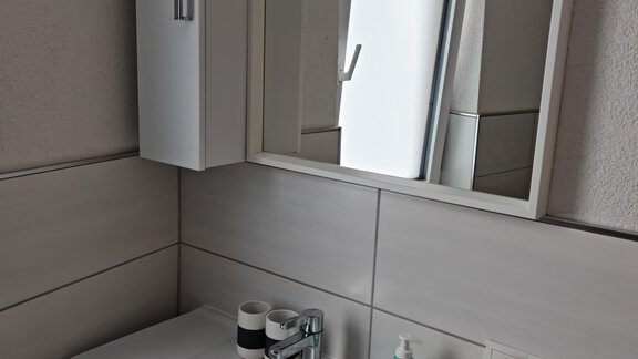 Ein modernes Badezimmer mit einem weißen Waschbecken und Spiegel. Die Wände sind hell gefliest und es gibt einige Pflegeprodukte auf der Ablage. - Apart Stefan - Niederthai