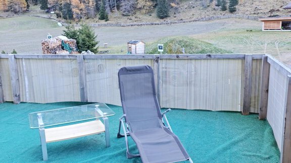 Eine Terrasse mit einem Liegestuhl und einem Glastisch. Im Hintergrund sind Bäume und eine Berglandschaft zu sehen. - Apart Stefan - Niederthai
