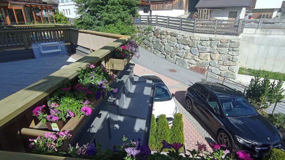 A beautiful driveway with two cars and colorful flower boxes. In the background, there are houses and a stone wall. - Appartement Lea - Niederthai