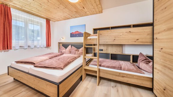 A cozy bedroom with a double bed and a bunk bed. The warm wooden furniture and the windows create an inviting atmosphere. - Appartement Lea - Niederthai
