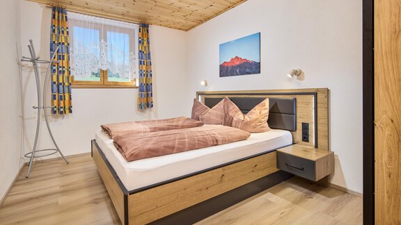 A modern bedroom with a double bed and wooden paneling. Large windows let in plenty of light and a picture on the wall creates atmosphere. - Appartement Lea - Niederthai