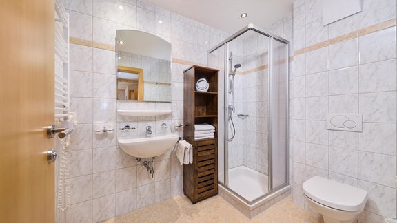 A modern bathroom with a shower, a sink, and a toilet. The room is brightly tiled and well-lit. - Appartement Lea - Niederthai