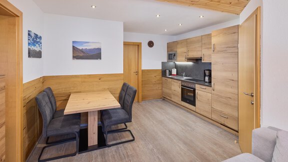 A modern kitchen corner with wood paneling and a dining area. The equipment includes a stove, a coffee machine, and a dining table with chairs. - Appartement Lea - Niederthai