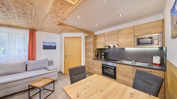 A modern kitchen with wood paneling and a cozy living area. The space is bright and inviting, ideal for relaxed days. - Appartement Lea - Niederthai