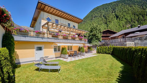 A cozy house surrounded by green lawn and trees. The terrace is equipped with loungers and flowers decorate the balconies. - Appartement Lea - Niederthai