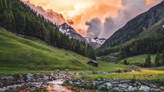 A picturesque landscape with a clear stream, surrounded by green meadows and mountains. The sky glows in warm colors at sunset. - Appartement Lea - Niederthai