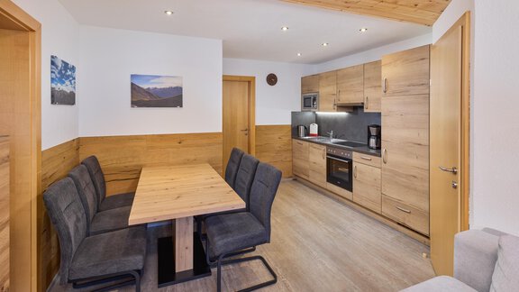 A modern kitchen with a wooden dining area. The walls are light, and there are some pictures of mountains. - Appartement Lea - Niederthai