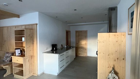 A bright and modern kitchen with wooden shelves and a small Christmas tree. The room feels inviting and spacious. - Delano Appartements - Niederthai