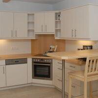 A modern kitchen with white cabinets and wooden surfaces. It is well equipped with an oven and a bar area. - Delano Appartements - Niederthai