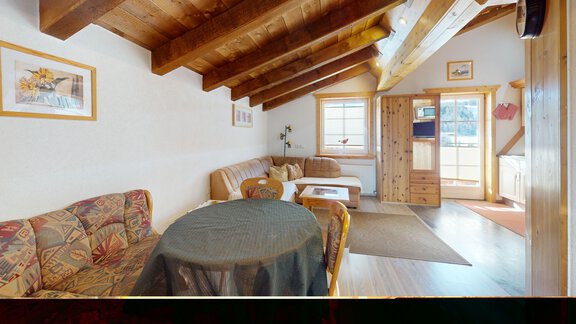 Ein gemütlicher Wohnraum mit Holzdecken und einem einladenden Sofa. Es gibt einen Tisch und viel natürliches Licht durch die Fenster. - Gipfelblick Appartements - Niederthai