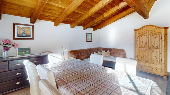 Ein gemütlicher Essbereich mit einem Holztisch und weißen Stühlen. Das Zimmer hat sichtbare Holzbalken und eine warme, einladende Atmosphäre. - Gipfelblick Appartements - Niederthai