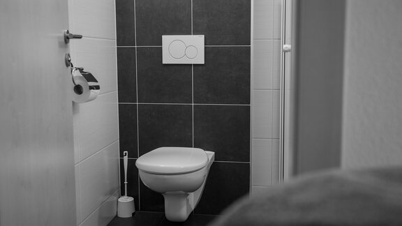 Ein einfaches Badezimmer mit einer weißen Toilette und modernen Fliesen. Die Wände sind teilweise gefliest und der Raum wirkt minimalistisch. - Sonnenhof - Niederthai