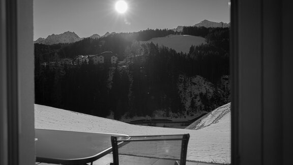 Ein ruhiger Blick auf verschneite Berge mit der Sonne hoch am Himmel. Ein Tisch und ein Stuhl sind im Vordergrund sichtbar. - Sonnenhof - Niederthai