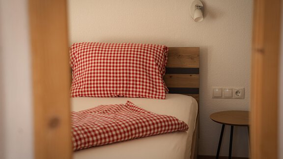 Ein gemütliches Schlafzimmer mit einem Bett und einem karierten Kopfkissen. Neben dem Bett steht ein kleiner Nachttisch. - Sonnenhof - Niederthai