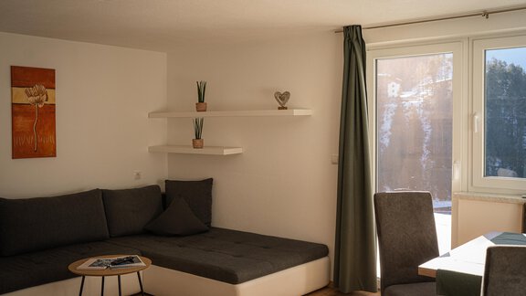 Ein modernes Wohnzimmer mit einer gemütlichen Couch und einem Tisch. Große Fenster sorgen für viel Licht und einen Blick nach draußen. - Sonnenhof - Niederthai
