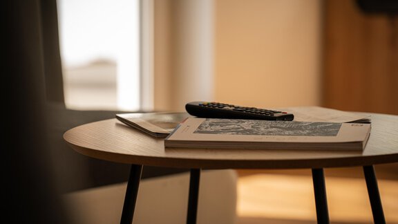 Ein Holztisch mit einem Magazin und einer Fernbedienung. Im Hintergrund ist ein helles Zimmer mit einem Fenster zu sehen. - Sonnenhof - Niederthai
