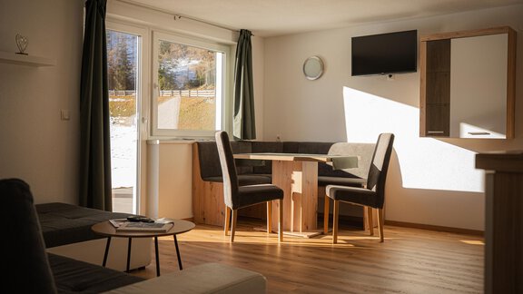 Ein modernes Wohnzimmer mit einem Tisch und Stühlen sowie einem Sofa. Großen Fenstern lassen viel Tageslicht herein. - Sonnenhof - Niederthai