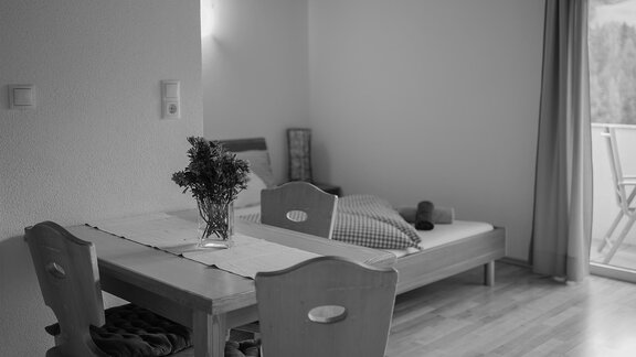 Ein einfaches Zimmer mit einem Tisch und Stühlen sowie einem Bett. Auf dem Tisch steht eine Vase mit Blumen. - Sonnenhof - Niederthai