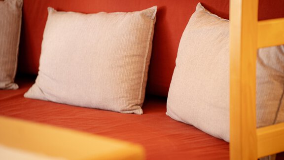 Ein gemütliches Sofa mit beige Kissen auf einem roten Stoffbezug. Die Atmosphäre ist einladend und entspannend. - Sonnenhof - Niederthai