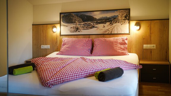 Ein gemütliches Schlafzimmer mit einem großen Bett und karierten Bettwäsche. An der Wand hängt ein Landschaftsbild und die Einrichtung ist aus Holz. - Sonnenhof - Niederthai