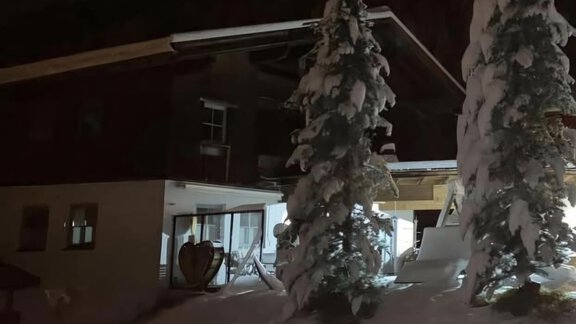 A snow-covered house at night, surrounded by tall, snow-covered firs. The lighting creates a cozy atmosphere. - Appartementhaus Schalfblick - Obergurgl 