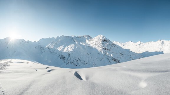 A vast, snow-covered mountain landscape under a clear blue sky. The sun shines over the snow-covered peaks. - Appartementhaus Schalfblick - Obergurgl 