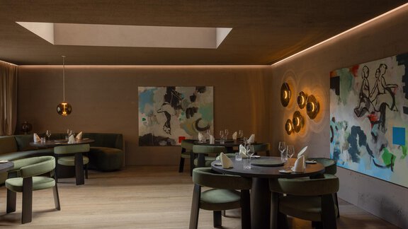 A modern restaurant with elegant round tables and stylish green chairs. Colorful artworks hang on the walls, and the lighting creates a cozy atmosphere. - Austria Gourmet & Wine Hotel - Obergurgl 