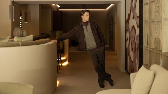 A stylishly dressed man leans relaxed against a modern piece of furniture in an elegant room. The soft lighting and minimalist decor create a pleasant atmosphere. - Austria Gourmet & Wine Hotel - Obergurgl 