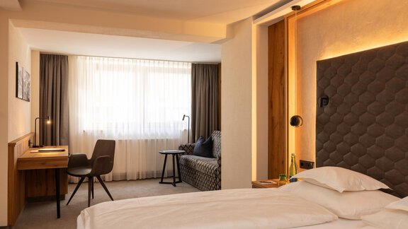 A modern hotel room with two beds and a cozy seating area. Large windows provide plenty of daylight and a pleasant atmosphere. - Austria Gourmet & Wine Hotel - Obergurgl 