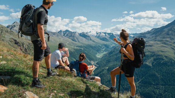 A group of hikers looks down from a mountainside onto a picturesque valley and the surrounding mountains. The environment is green and sunny, ideal for outdoor activities. - Chalet Cecilia by MYALPS - Obergurgl 