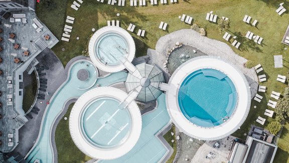 A modern pool area with multiple pools and lounges. The view is from a bird's eye perspective, surrounded by green lawns. - Chalet Cecilia by MYALPS - Obergurgl 