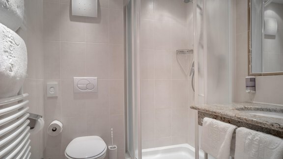 A modern bathroom with shower, toilet, and sink. The walls are kept in a bright white, and there are towels as well as a towel warmer. - Ferienwohnung de Luxe Alpenresidenz am Mühlbach - Obergurgl 