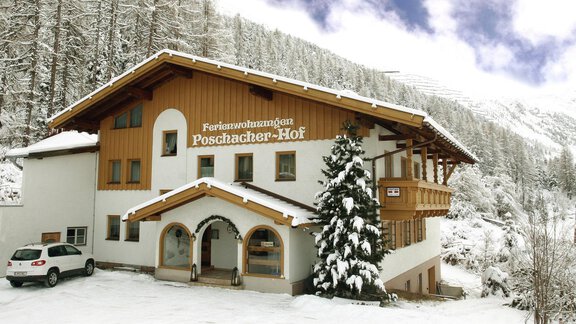 A charming wooden house in the snow, surrounded by a wintry landscape. The façade is pleasantly designed, with a large window and a tree covered in white snow. - Ferienwohnung Poschacherhof - Obergurgl 