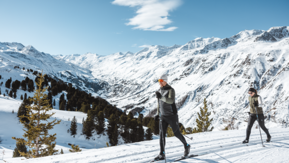 Two people are hiking in the snow in the mountains. The landscape is adorned with snow-covered peaks and trees. - Forest Chalet - Obergurgl 