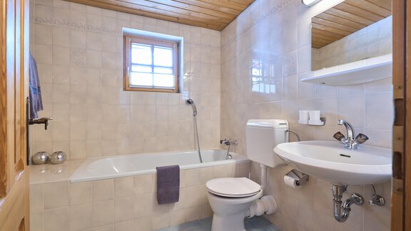 A bright bathroom with a bathtub and a modern sink. Wooden ceilings and a small window create an inviting atmosphere. - Forest Chalet - Obergurgl 