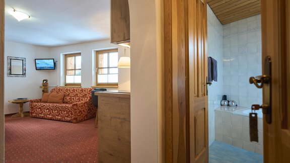 A cozy room with a red sofa and a flat-screen TV. In the background, a bathroom with a bathtub is visible. - Forest Chalet - Obergurgl 