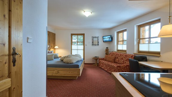 A cozy room with a double bed and a red sofa. The room has large windows and a warm, inviting atmosphere. - Forest Chalet - Obergurgl 