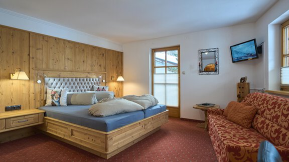 A cozy room with a double bed and a sofa. The walls are made of wood, and there is a television as well as windows with natural light. - Forest Chalet - Obergurgl 