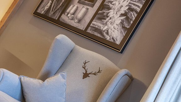A cozy armchair with a deer antler motif and a cushion. In the background, black-and-white pictures can be seen on the wall. - Gletscherblick - Serviced Apartments - Obergurgl 