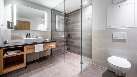 A modern bathroom with a glass shower and an elegant wooden dresser. The walls are done in neutral tones, creating a bright and inviting atmosphere. - Gletscherblick - Serviced Apartments - Obergurgl 