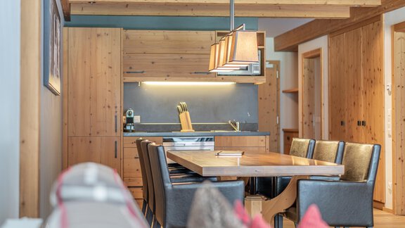 A modern kitchen with wooden cabinets and a large dining table. The decor is bright and friendly, with wood details and elegant chairs. - Gletscherblick - Serviced Apartments - Obergurgl 
