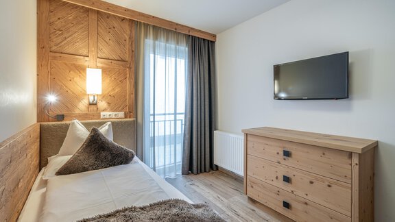 A modern room with wooden paneling, a single bed, and a flat-screen TV. Large window area with balcony access and a cozy atmosphere. - Gletscherblick - Serviced Apartments - Obergurgl 