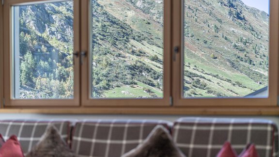 A cozy room with a view of green hills and mountains. The windows let in plenty of light and provide a beautiful view. - Gletscherblick - Serviced Apartments - Obergurgl 