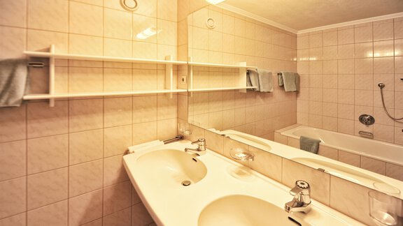A bright bathroom with two sinks and a large mirror. The walls are tiled in white, and towels hang on a shelf. - Haus Timmelseck - Obergurgl 