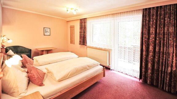 A cozy bedroom with two beds and soft pillows. The large windows provide plenty of daylight and a view of the outdoors. - Haus Timmelseck - Obergurgl 