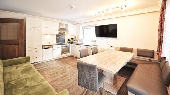 A modern kitchen with a large dining table and cozy seating. The bright living room features a television and an open floor plan. - Haus Timmelseck - Obergurgl 