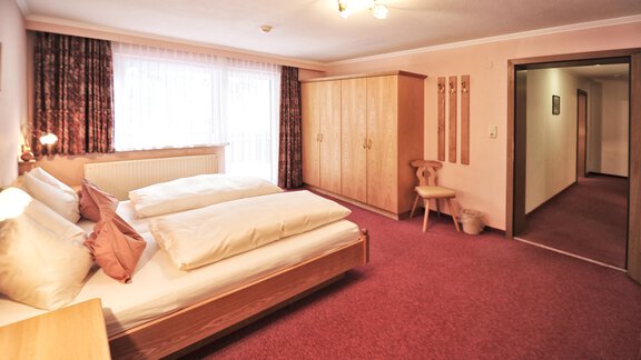A cozy bedroom with two beds and a wooden wardrobe. The room has large windows and a warm, inviting carpeted floor. - Haus Timmelseck - Obergurgl 