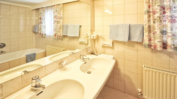 A bright bathroom with two sinks and a large mirror. The walls are tiled and there is a bathtub as well as towels in soft colors. - Haus Timmelseck - Obergurgl 