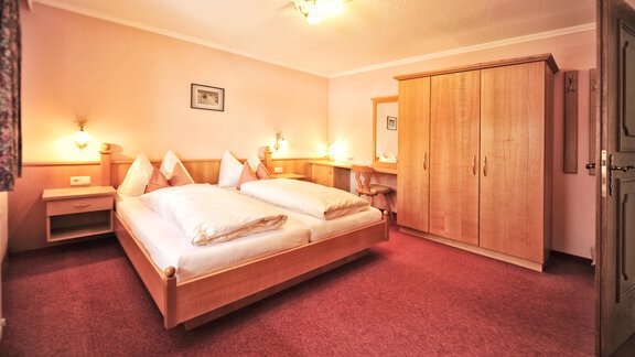 A cozy bedroom with two single beds and warm lighting. The room is designed in soft colors and contains a wardrobe as well as a table. - Haus Timmelseck - Obergurgl 